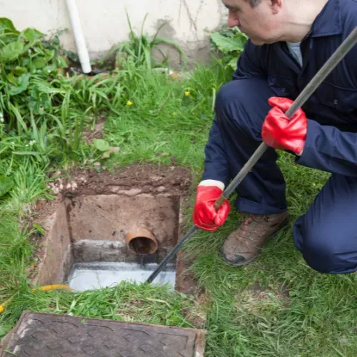 Technician clearing a blocked outdoor drain with a rod.